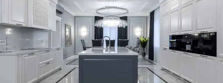 White kitchen cabinetry surrounding a blue-gray island with chandelier lighting
