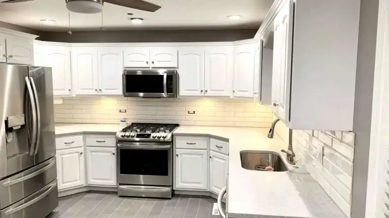 White kitchen cabinets around a stainless steel stove and microwave with pale countertops