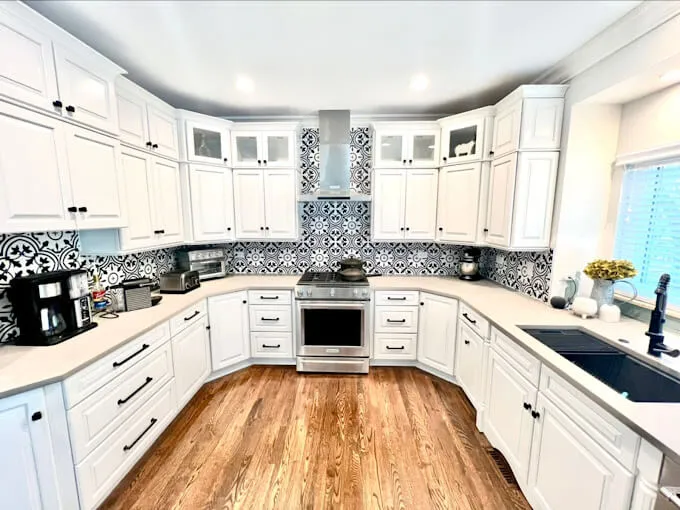 Refinished white kitchen cabinets with a patterned tile backsplash and range hood in a Chicago-area home