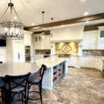 White painted kitchen cabinets with a large island, range hood and chandelier