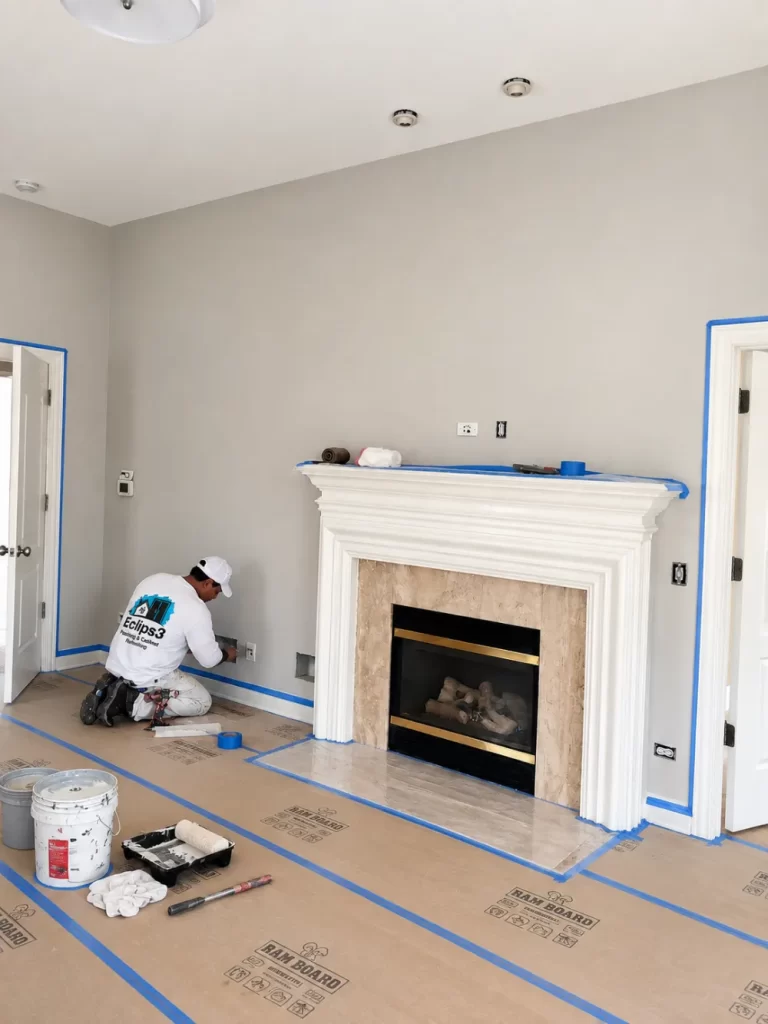 Painter taping and painting the trim and fireplace mantel in a living room