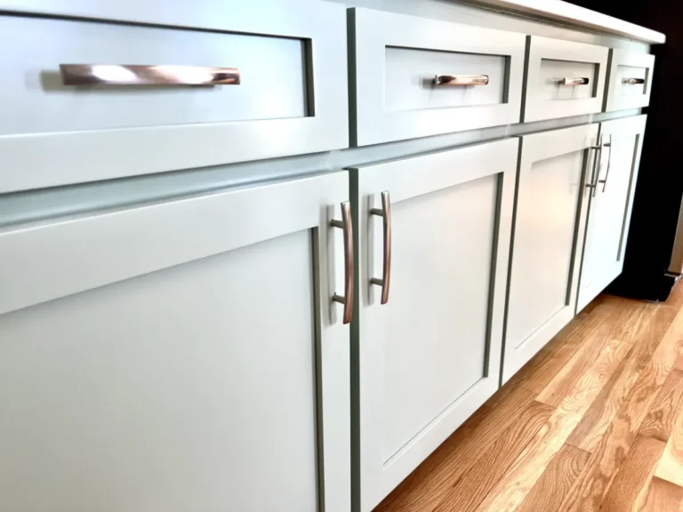 Close-up of finished light-gray cabinet doors and drawers with brushed metal handles