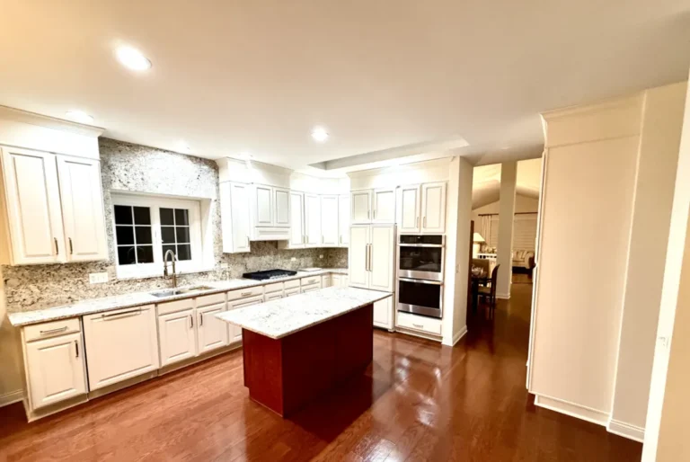 Wide view of white kitchen cabinets, granite counters and a wood-toned center island