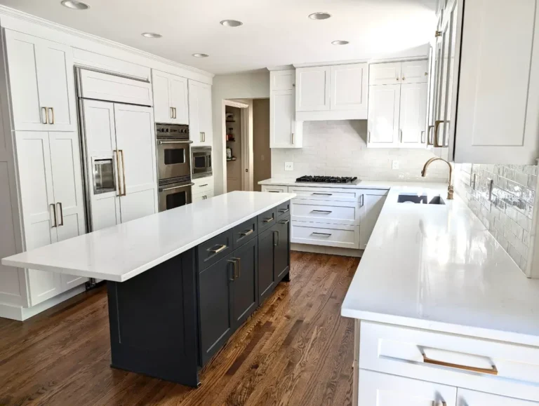 White kitchen cabinets with a charcoal island, pale countertops and wood flooring