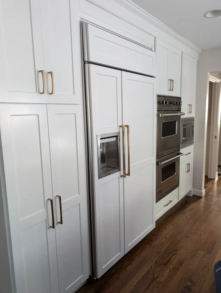 White paneled refrigerator surround and tall kitchen cabinets with brass handles