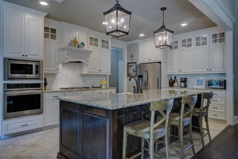 White kitchen cabinets with glass-front upper doors, a dark island and lantern pendant lights